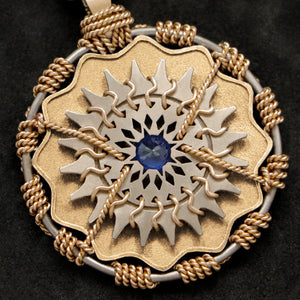 Detail view of 18K Yellow Gold and 18K Palladium White Gold and Sapphire Sewn Gold Metal Majesty pendant featuring 20 pointed gear by Caps Brothers