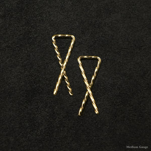 Laying down pair of 18K Yellow Gold Sibling Ribbons Twisted Earrings representing we are all brothers and sisters by Caps Brothers