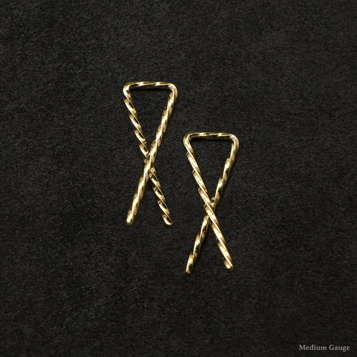 Laying down pair of 18K Yellow Gold Sibling Ribbons Twisted Earrings representing we are all brothers and sisters by Caps Brothers