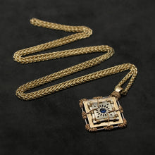 Load image into Gallery viewer, Laying down view of 18K Yellow Gold and 18K Palladium White Gold and Sapphire Sewn Gold Metal Confidence pendant and chain with endless loop necklace featuring 4 pointed gear by Caps Brothers