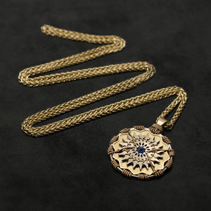Laying down view of 18K Yellow Gold and 18K Palladium White Gold and Sapphire Sewn Gold Metal Majesty pendant and chain with endless loop necklace featuring 20 pointed gear by Caps Brothers